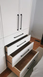 White closet with slim shaker style door & drawer fronts and  black handles in a room with wooden flooring.