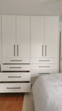 White closet with slim shaker style door & drawer fronts and  black handles in a room with wooden flooring.