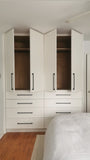 White closet with slim shaker style door & drawer fronts and  black handles in a room with wooden flooring.