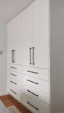 White closet with slim shaker style door & drawer fronts and  black handles in a room with wooden flooring.