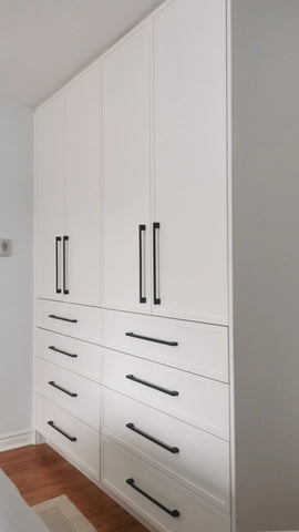 White closet with slim shaker style door & drawer fronts and  black handles in a room with wooden flooring.