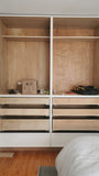 White closet with slim shaker style door & drawer fronts and  black handles in a room with wooden flooring.