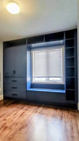 A custom floor-to-ceiling, wall-to-wall storage unit designed to frame a window. The design includes a spacious section featuring two doors and three drawers, perfect for keeping items out of sight. It also incorporates open shelving, which is ideal for displaying decor, books, bar essentials, or electronics. Additionally, the unit features a custom bench-cum-chest to provide both extra seating and integrated storage.