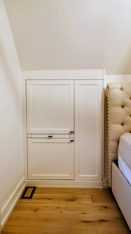 Custom-built angled cabinet designed for an unusual space under a sloped ceiling beside the bed, adding not only functional storage but also features a convenient pull-out nightstand.