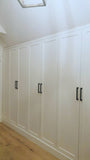 A closet design   specifically tailored to fit rooms with sloped or slanted ceilings, featuring beveled shaker doors. The design maximizes storage while creating both a functional and beautiful space.