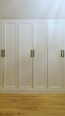 A closet design   specifically tailored to fit rooms with sloped or slanted ceilings, featuring beveled shaker doors. The design maximizes storage while creating both a functional and beautiful space.