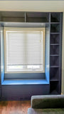 A custom floor-to-ceiling, wall-to-wall storage unit designed to frame a window. The design includes a spacious section featuring two doors and three drawers, perfect for keeping items out of sight. It also incorporates open shelving, which is ideal for displaying decor, books, bar essentials, or electronics. Additionally, the unit features a custom bench-cum-chest to provide both extra seating and integrated storage.