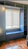 A custom floor-to-ceiling, wall-to-wall storage unit designed to frame a window. The design includes a spacious section featuring two doors and three drawers, perfect for keeping items out of sight. It also incorporates open shelving, which is ideal for displaying decor, books, bar essentials, or electronics. Additionally, the unit features a custom bench-cum-chest to provide both extra seating and integrated storage.