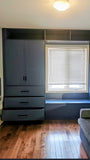 A custom floor-to-ceiling, wall-to-wall storage unit designed to frame a window. The design includes a spacious section featuring two doors and three drawers, perfect for keeping items out of sight. It also incorporates open shelving, which is ideal for displaying decor, books, bar essentials, or electronics. Additionally, the unit features a custom bench-cum-chest to provide both extra seating and integrated storage.