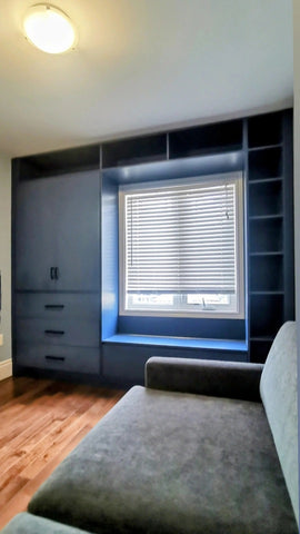 A custom floor-to-ceiling, wall-to-wall storage unit designed to frame a window. The design includes a spacious section featuring two doors and three drawers, perfect for keeping items out of sight. It also incorporates open shelving, which is ideal for displaying decor, books, bar essentials, or electronics. Additionally, the unit features a custom bench-cum-chest to provide both extra seating and integrated storage.