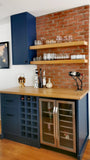 Kitchen island with blue cabinets, wooden shelves, and a brick wall backdrop.