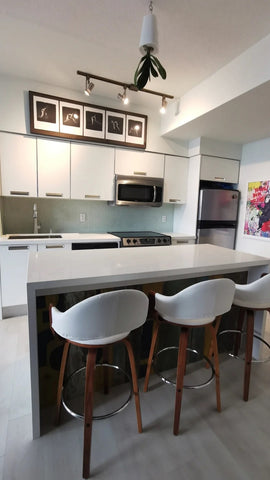 The waterfall island brings  style & functionality to this condo kitchen.  Not only adding a  large work surface  to cook  & entertainment but also lots of additional storage.  Double doors with deep adjustable  shelves  on either end and a large drawer in the middle for garbage & recycle bins.  The side facing the living room is clad with beautiful - one of kind - reclaimed teak panels.  The countertop on the kitchen side was replaced to match the island giving  kitchen a new life and look.